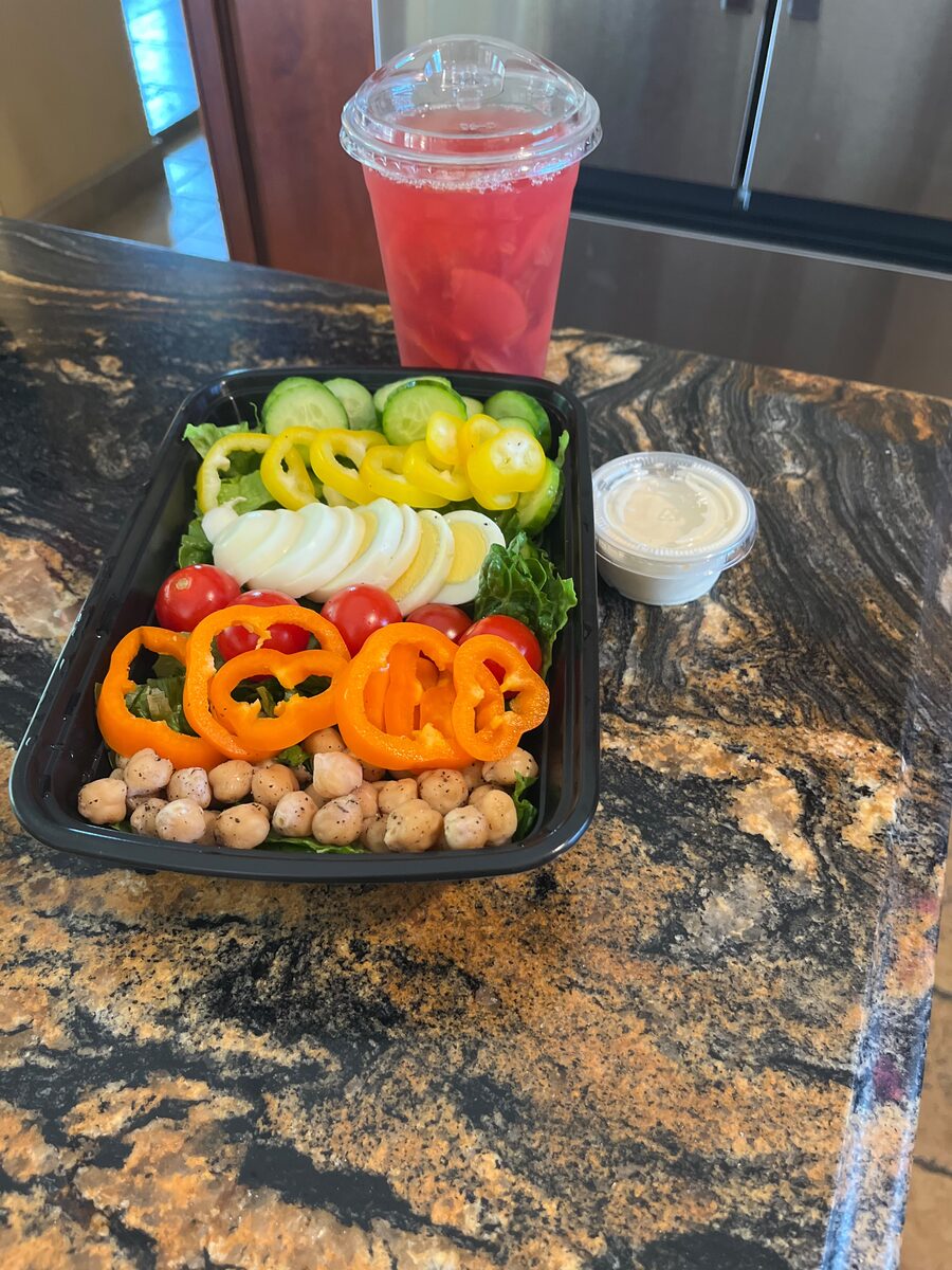 A colorful custom salad with tomato, bell pepper, egg, and chickpeas, served with a drink